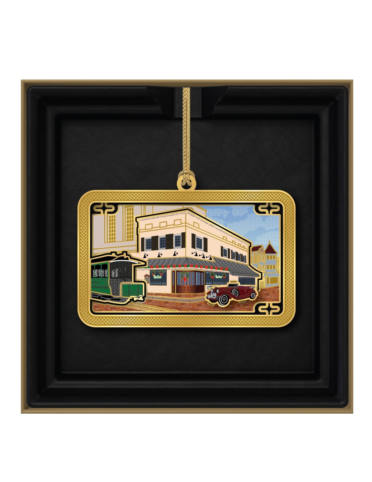 Decorative ornament with a building and trolley design in a gold frame, displayed in a black box.